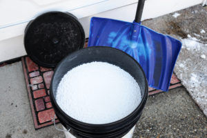Shovel and bucket of salt used to melt ice on driveway