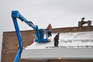 Workers shoveling snow manually off the roof of the building