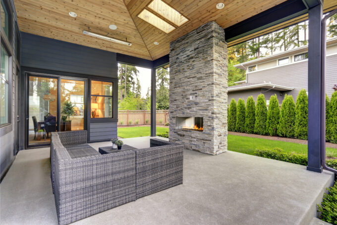 A modern enclosed patio with a stone-brick fireplace and a gray modular couch