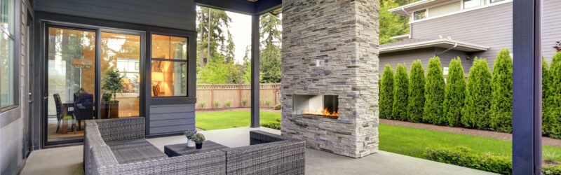 A modern enclosed patio with a stone-brick fireplace and a gray modular couch